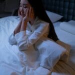 Azjatka leży bezsennie w łóżku nocą, zamyślona i przygnębiona