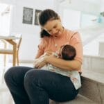 Uśmiechnięta mama przytula niemowlę, siedząc na schodach w domu